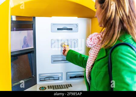 Femme vêtue d'un manteau vert, insérer la carte de crédit dans un guichet automatique Banque D'Images