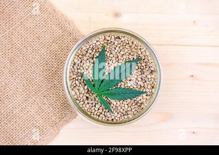 Graines de cannabis dans un bol en verre sur la table et le tissu de chanvre riche en protéines et en graisses saines Banque D'Images