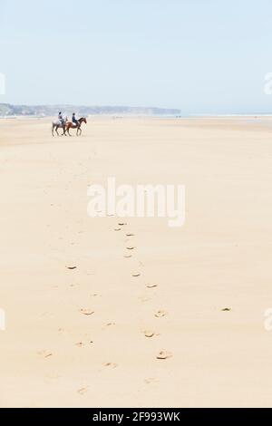 Empreintes de pas dans le sable d'Omaha Beach. Deux cavaliers avec leurs chevaux sur le chemin de l'eau. Banque D'Images