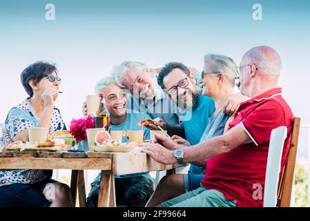 Joyeux groupe de famille fêtez ensemble en amitié avec plaisir et rire - les caucasiens apprécient la nourriture et les boissons pour la fête extérieur autour de la table - des générations mixtes de personnes âgées à jeune garçon Banque D'Images