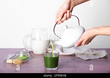 Femme versant le thé matcha de la théière dans le verre à la lumière arrière-plan Banque D'Images