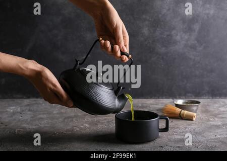 Femme versant le thé matcha de la théière dans la tasse à l'obscurité arrière-plan Banque D'Images