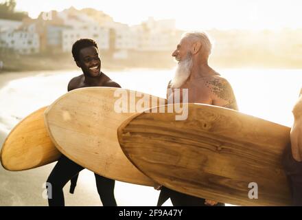 Des surfeurs heureux avec des âges et des courses différents s'amuser pendant la journée de surf sur la plage au coucher du soleil - Concept de mode de vie et d'amitié pour les sports extrêmes Banque D'Images