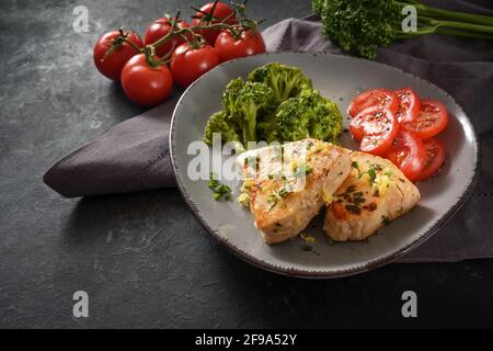 Filet de thon frit avec brocoli et tomates, zeste de persil et de citron sur une assiette grise et une table en ardoise sombre, espace de copie, foyer sélectionné et na Banque D'Images