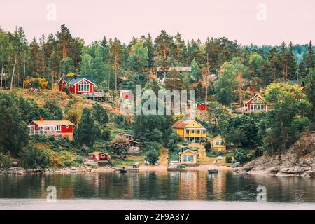 Suède. Beaucoup de belles chalets en bois suédois rouge et jaune Maisons sur la côte des îles Rocheuses en soirée d'été. Paysage de lac ou de rivière Banque D'Images