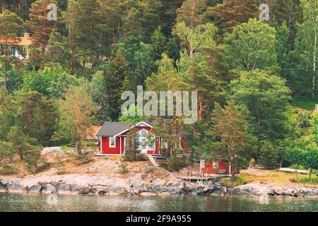 Suède. Magnifiques chalets en bois rouge ASwedish Maisons sur la côte des Rocheuses en été. Paysage de lac ou de rivière Banque D'Images