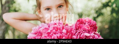 portrait d'une jolie petite fille caucasienne de sept ans, tient dans les mains un bouquet de fleurs de pivoine rose en pleine fleur et la redressant Banque D'Images