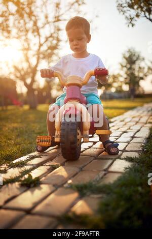 Un petit garçon en train de faire du vélo dans la cour de la ferme par une belle journée ensoleillée. Ferme, campagne, été Banque D'Images