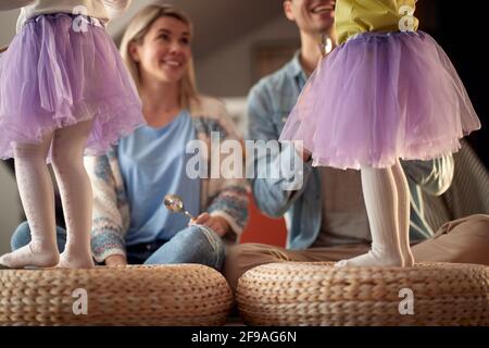 Maman et papa drumming sur le mobilier tandis que leurs petites filles dansent dans une atmosphère gaie à la maison. Famille, maison, jouer, ensemble Banque D'Images