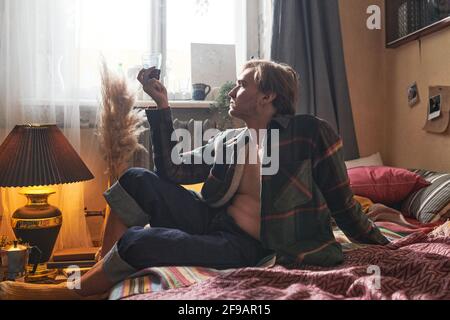 Jeune homme assis sur le sol et tenant le verre de vin rouge dans sa main dans la chambre intérieure à la maison Banque D'Images