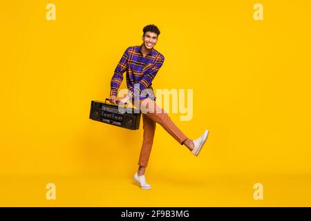 Portrait complet de drôle insouciante peau sombre homme danse les mains portent une boombox isolée sur fond jaune Banque D'Images