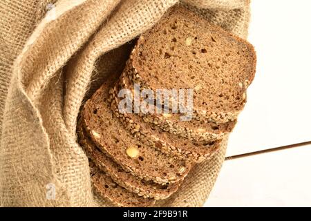 Quelques morceaux de pain frais parfumé, savoureux, au sésame dans un sac de jute, en gros plan, sur une table peinte en bois. Banque D'Images