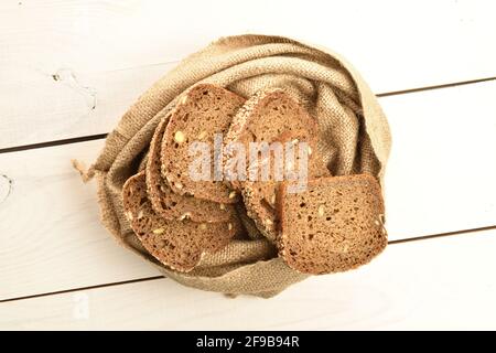 Quelques morceaux de pain frais parfumé, savoureux, au sésame dans un sac de jute, en gros plan, sur une table peinte en bois. Banque D'Images