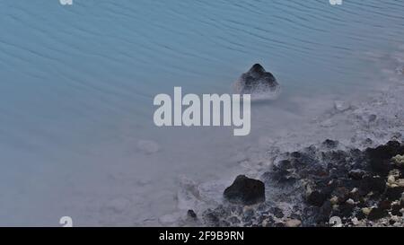 Vue rapprochée de la piscine avec eau chaude de couleur bleue et rochers de lave noirs avec dépôts de minéraux blancs près de la station thermale Blue Lagoon en Islande. Banque D'Images
