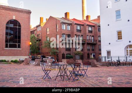 Tables avec chaises et pieds métalliques dans une place déserte entouré de bâtiments résidentiels en briques rénovés au coucher du soleil Banque D'Images