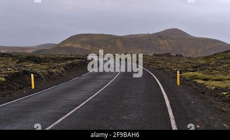 Perspective décroissante de la route sinueuse de pays avec des marques entre les champs de lave couverts de mousse de pierres volcaniques près de Grindavik, Reykjanes, Islande. Banque D'Images