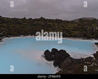 Piscine avec eau thermale bleue chatoyante entourée d'un champ de lave couvert de mousse près de la station thermale géothermique Blue Lagoon à Grindavik, Reyjanes, Islande. Banque D'Images