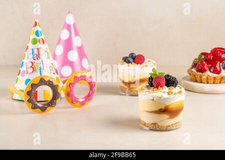 Desserts sucrés avec baies fraîches et chapeau d'anniversaire sur fond lumineux. Banque D'Images