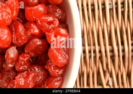 Quelques cerises rouges, naturelles, biologiques, douces et aigres séchées dans un bol en céramique blanche sur un panier en osier. Banque D'Images