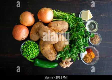 Pommes de terre Samosa Ingrédients sur un fond de bois foncé : pommes de terre crues, oignons, pois, herbes et épices sur une table en bois Banque D'Images