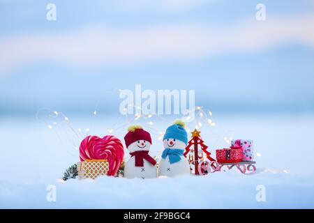 Amis bonhommes de neige restent avec un traîneau et une boîte cadeau sur la neige éclairée par des lumières de fées. Bonbons rouges à coeur blanc. Bonne Année. Composition de Noël. Banque D'Images