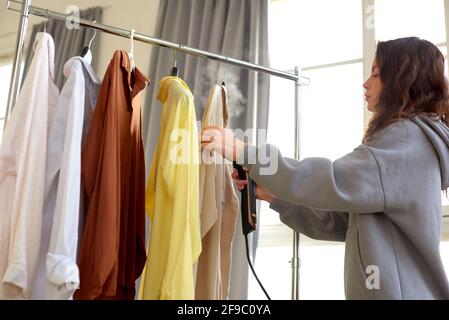 Une fille vole des vêtements sur un cintre. Femme avec défroisseur de vêtements de nettoyage dans le salon de nettoyage à sec Banque D'Images