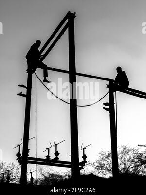 silhouette noire et blanche d'un deux homme assis sur un poteau électrique. Banque D'Images