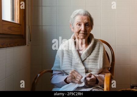 la grand-mère se penche avec l'aiguille et le fil tout en regardant la caméra Banque D'Images