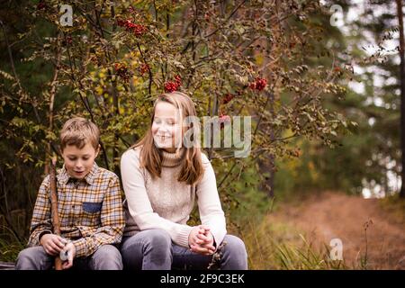 Deux adolescents blonds, une fille et un garçon, une sœur et un frère s'assoient dans la forêt d'automne et s'amusent à discuter. Banque D'Images