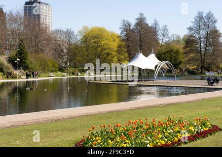 Le kiosque couvert et le lac nautique dans le parc d'Eastrop avec des fleurs de printemps en premier plan et le bâtiment AA en arrière-plan. Basingstoke, Royaume-Uni Banque D'Images