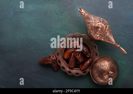 Plaque de bronze avec dates et lampe aladdin sur fond en bois peint vert foncé avec espace vide pour le texte . Pose à plat. Arrière-plan du ramadan. Ramadan Banque D'Images