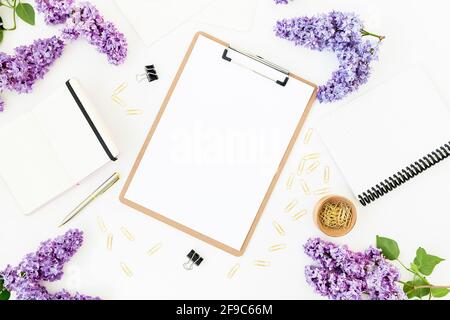 Composition de bureau à domicile avec presse-papiers, agenda, fleurs lilas et accessoires sur fond blanc. Flat lay, vue de dessus. Banque D'Images