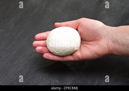 Un morceau de fromage mozzarella fraîchement préparé dans une femelle paume sur fond noir avec une ombre sombre Banque D'Images