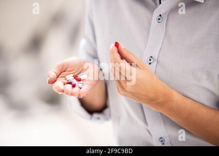 Diverses pilules dans une main d'une femelle avec l'autre main tenant une pilule rouge entre un pouce et un doigt. Banque D'Images