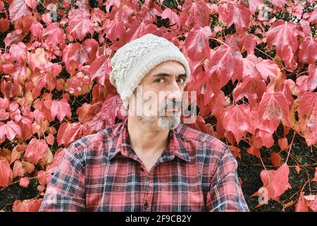 Portrait d'un homme caucasien mûr vêtu d'une chemise à carreaux et d'une casquette en laine avec un fond de feuilles automnales. Banque D'Images