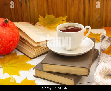 Atmosphère d'automne. Une tasse de thé, des feuilles d'érable jaune, des livres et une chose tricotée Banque D'Images