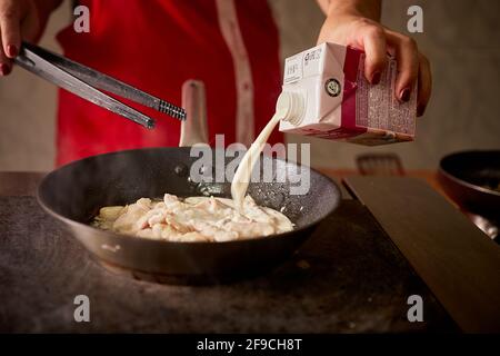 verser à la main de la crème de lait dans une poêle avec des crevettes coller Banque D'Images