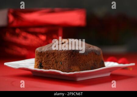 Gâteau de prune, délicieux gâteau de christmus fait maison en utilisant des raisins secs, noix de cajou et fruits secs qui est carré dans la forme placée sur la vaisselle blanche avec rouge Banque D'Images