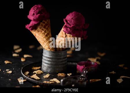 Gros plan de deux cônes de glace violets sur un contenant en métal entouré de morceaux de gaufres cassés Banque D'Images