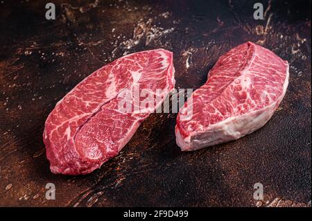 Lame supérieure brute ou steaks de viande de bœuf en fer plat sur une table de boucher. Arrière-plan sombre. Vue de dessus Banque D'Images