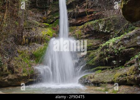 L'eau puissante d'une chute d'eau qui éclabousse les rochers d'une falaise humides et vert vif au début du printemps Banque D'Images