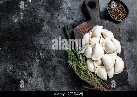 Boulettes crues pierogi congelées avec pomme de terre sur une planche de bois. Arrière-plan noir. Vue de dessus. Copier l'espace Banque D'Images