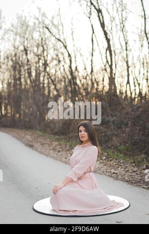 Photo verticale d'une femme caucasienne assise sur un film réflecteur sur la route entourée d'arbres Banque D'Images