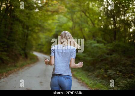 Dos d'une femme en chemise grise et jeans qui marche sur un petit chemin dans la forêt Banque D'Images