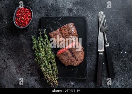 Top Blade grillé ou biftecks de viande de bœuf rôti en fer plat sur un plateau en marbre. Arrière-plan noir. Vue de dessus Banque D'Images