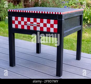 Table de chevet noire avec tiroir qui a été repeint et peint avec de la peinture à la craie Annie Sloan. Le tiroir est peint en rouge et blanc à carreaux. Banque D'Images