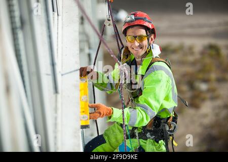 Grimpeur industriel gai mesurant avec un tube de niveau pendant les travaux de construction Banque D'Images