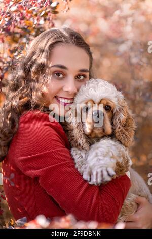 Jolie jeune femme qui embrasse le chien d'épagneul américain de cocker dans la nature dans le parc sur fond de feuilles automnales Banque D'Images