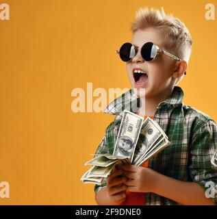 Garçon blond riche en lunettes de soleil rondes et carreaux les chemises sont dotées d'un fan de dollars en argent dans les mains et hurle Banque D'Images