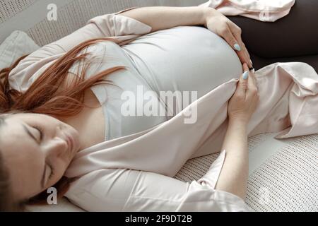 Femme enceinte élégante au cours du dernier mois se reposant sur le canapé à la maison de près. Banque D'Images